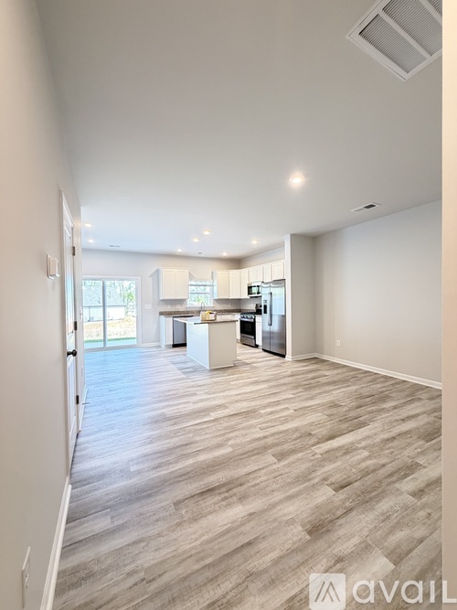 A spacious room with wooden flooring and a kitchen area in the background.