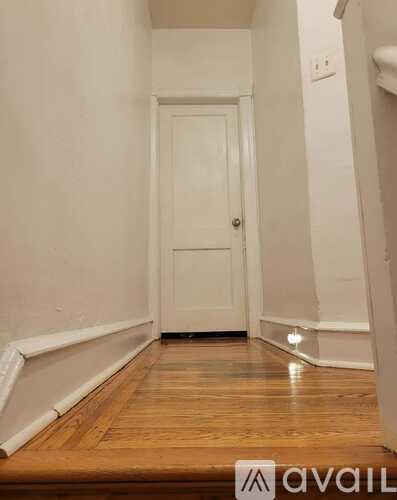 A hallway with a white door and wooden floor.