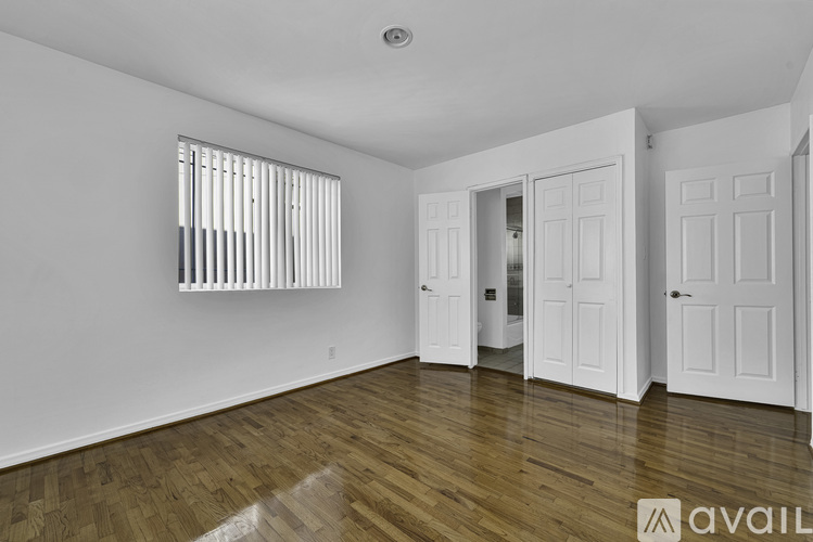 A room with wooden floors and white walls, with a window and a door visible.