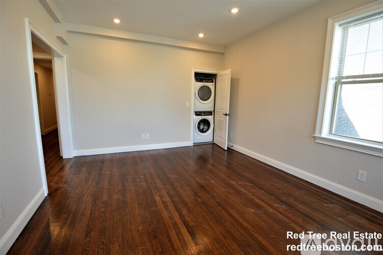 A room with wood flooring and a washer and dryer stacked in the corner.