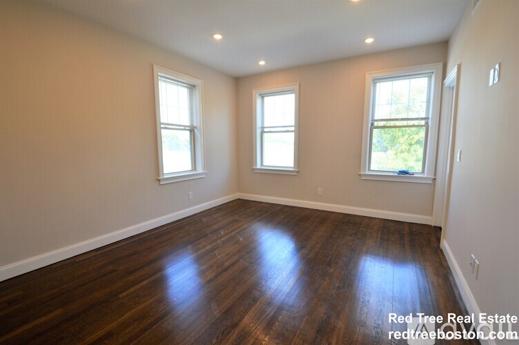 A room with wooden floors and three windows.