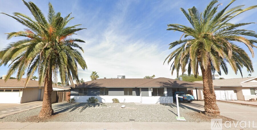 A house with a gravel driveway and two palm trees in front.