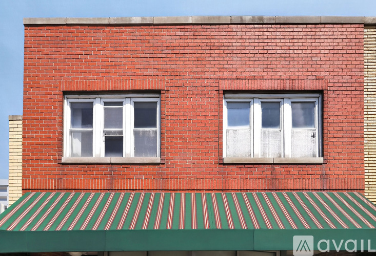A red brick building with two windows and a green striped awning.