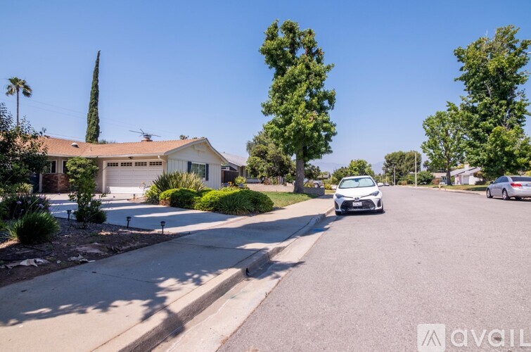 A car is parked on a street with a house and trees in the background.