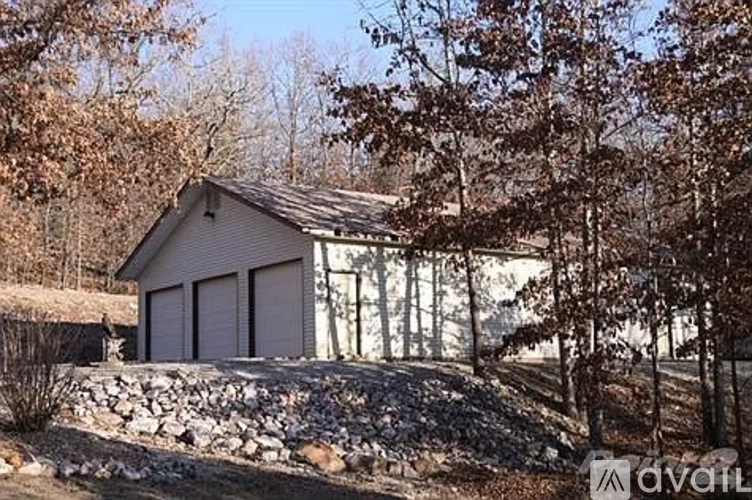 A small house with a grey roof and two white garage doors is surrounded by trees.