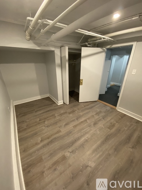 A room with wooden flooring and white walls, with a doorway leading to another room.