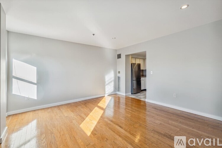 A spacious room with wooden flooring and a large window on the left side.