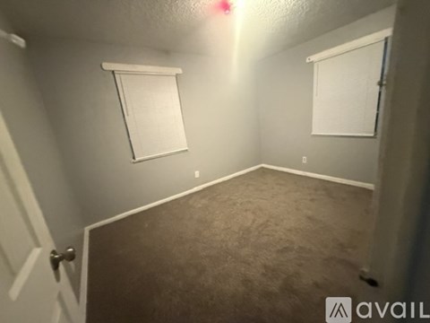 A room with carpeted floor, two windows with blinds, and a door.