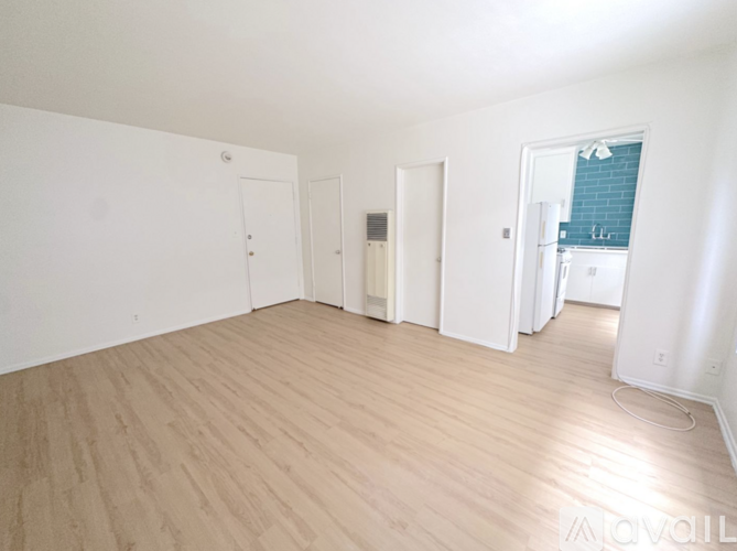A room with white walls and wooden flooring, with a door on the left and a window on the right.