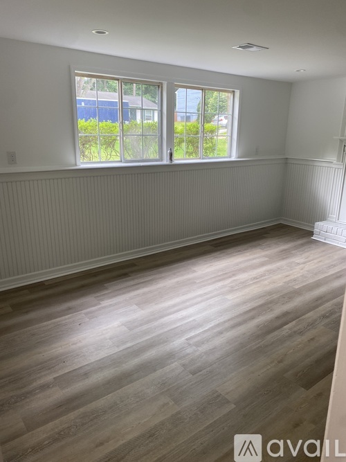 A room with wooden flooring and a window overlooking a blue fence.