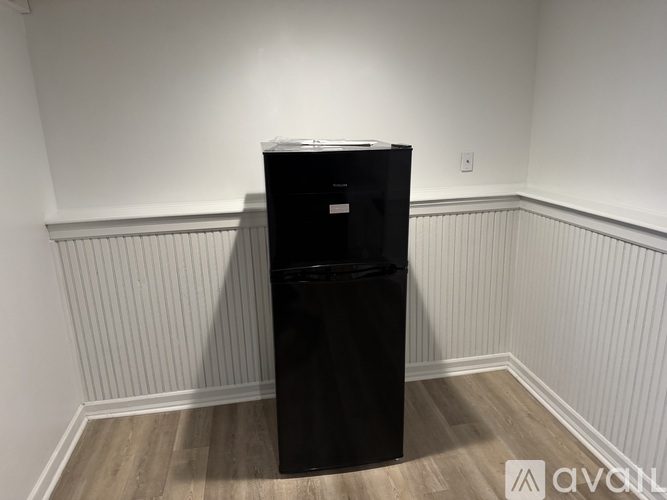 A black fridge in a room with wooden flooring and white walls.