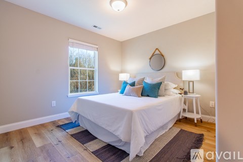 A bedroom with a white bed and a window with a view of trees outside.