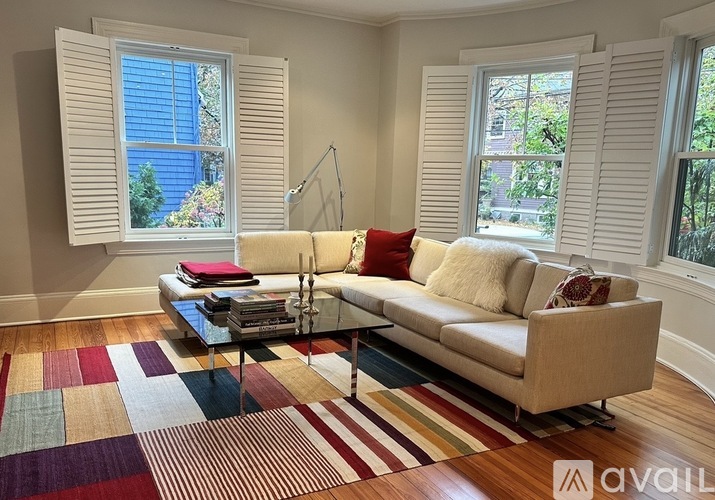 A living room with a beige couch, a glass coffee table, and a colorful rug.