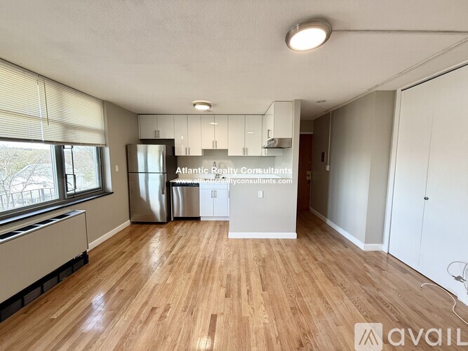 A spacious room with wooden flooring and a window overlooking a tree-lined street.