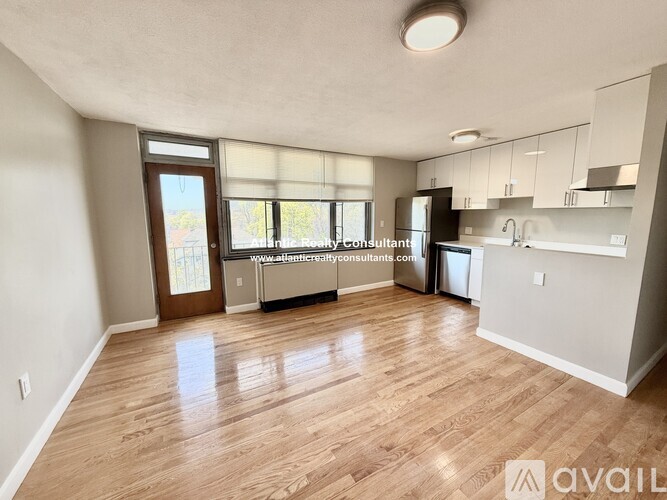 A well-lit, spacious kitchen and living room with wooden flooring and white walls.
