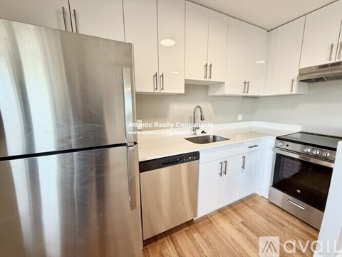 A modern kitchen with a stainless steel refrigerator and wooden flooring.