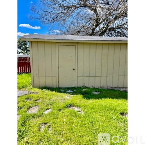 A shed with a door and windows is surrounded by grass and rocks.