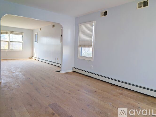 A room with wooden flooring and white walls, with a window on the right side.