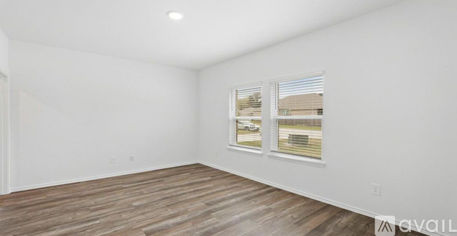 A room with white walls and wooden flooring, with a window showing a view of a building and a fence.