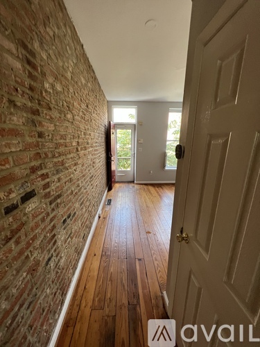 A hallway with a brick wall and wooden floors leading to a door.