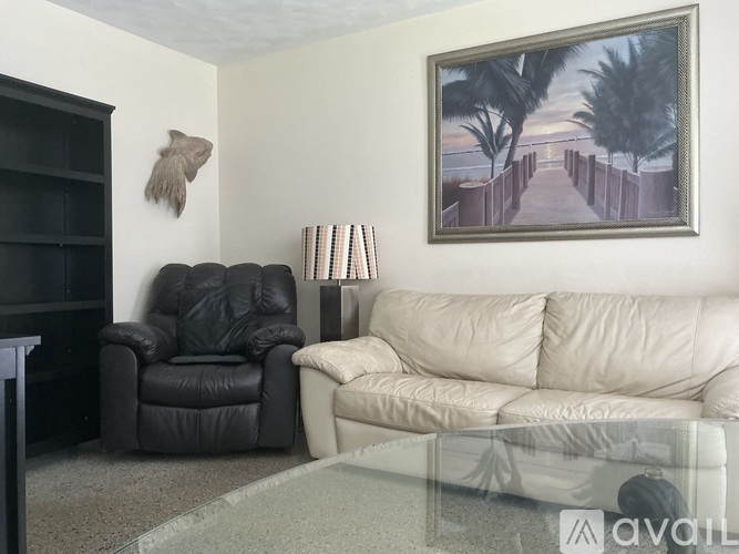 A living room with a black leather chair, a white couch, and a painting on the wall.