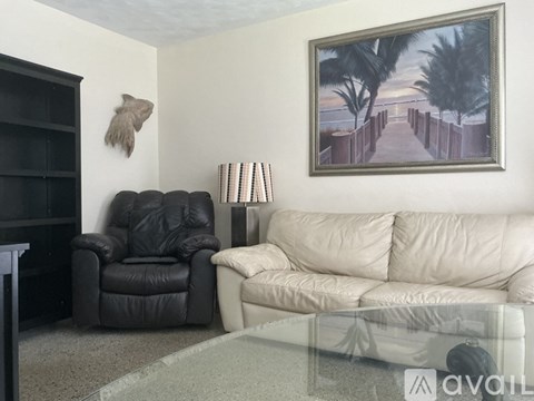 A living room with a black leather chair, a white couch, and a painting on the wall.