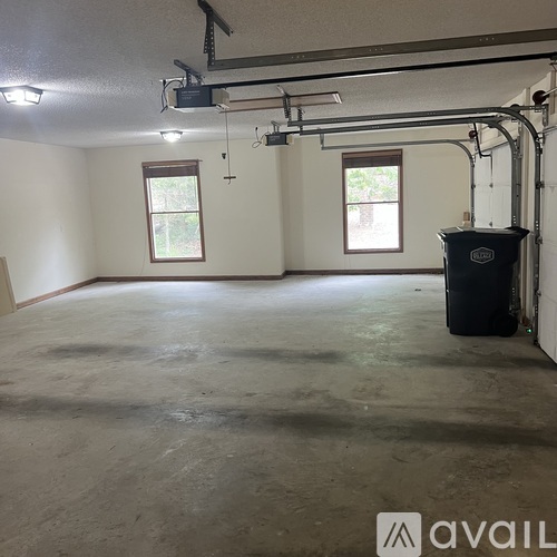 A spacious garage with a concrete floor and a black trash can.