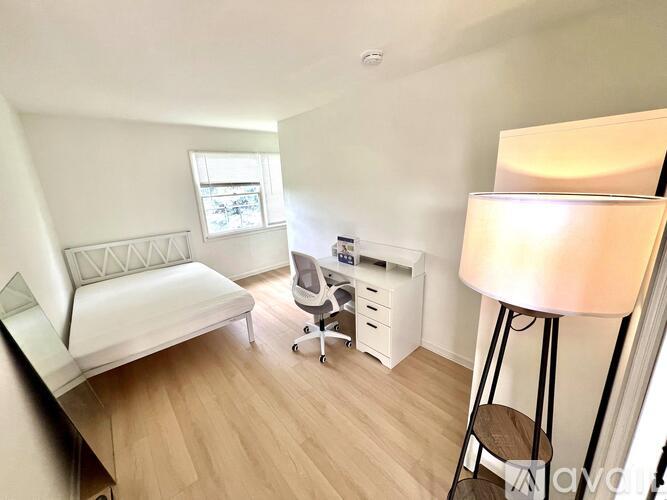 A white bedroom with a bed, desk, and chair.