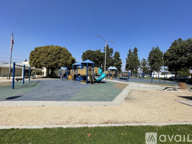 A playground with a blue and green slide, a sandbox, and a flagpole with an American flag.