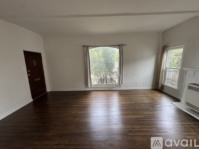 A room with wooden flooring and a window with a view of trees.