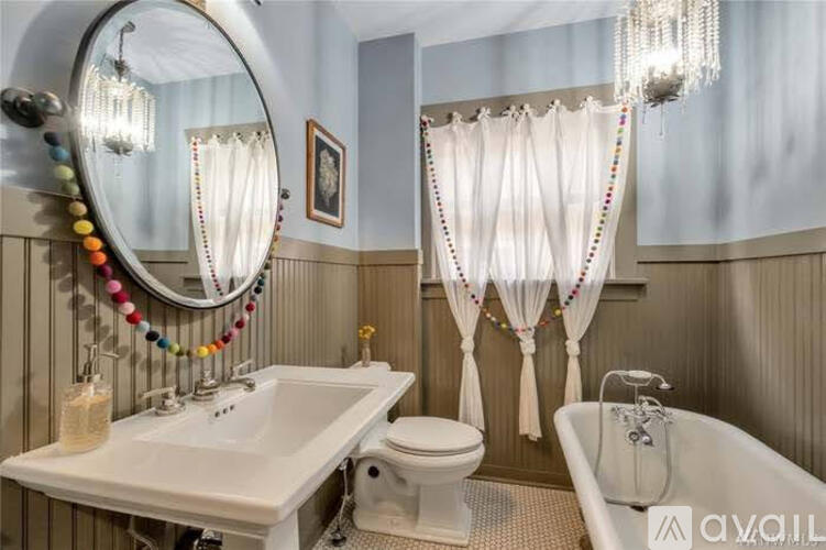 A bathroom with a white sink, toilet, and bathtub, decorated with a colorful beaded garland.