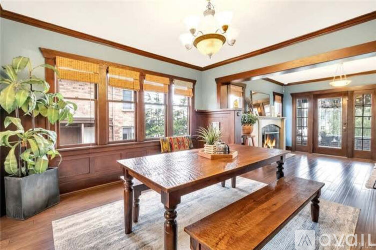 A large wooden dining table is surrounded by benches in a spacious room with a fireplace and a potted plant.