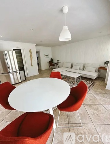 A white table with red chairs is in the middle of a white room.