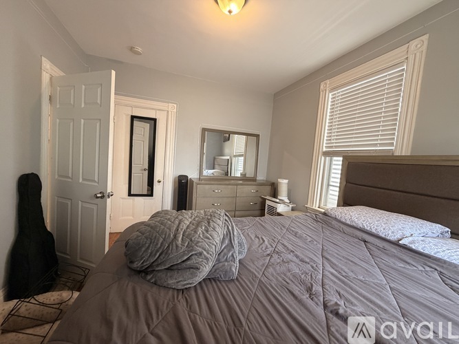 A bedroom with a bed covered in a grey blanket and a mirror on the wall.
