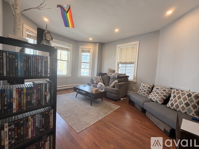 A living room with a bookshelf filled with books on the left side and a grey sofa in the center.