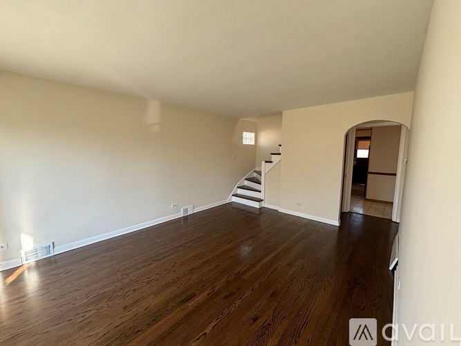A room with wooden floors and a staircase in the background.