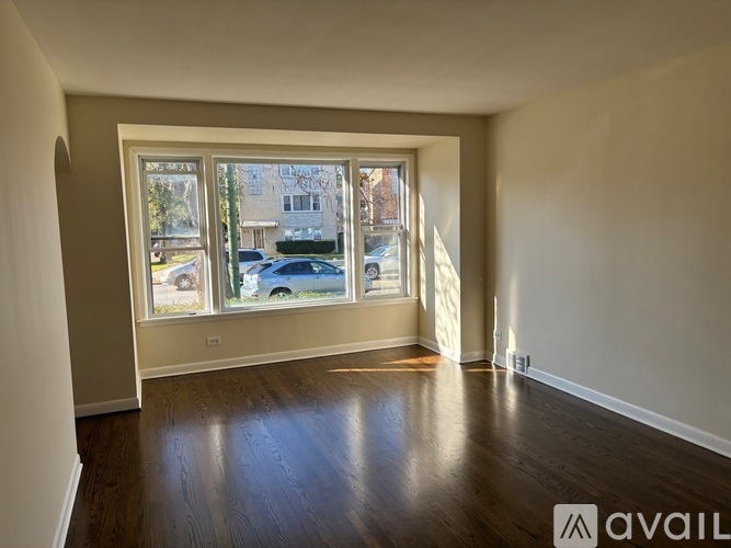 A room with wooden floors and a large window showing a street view.