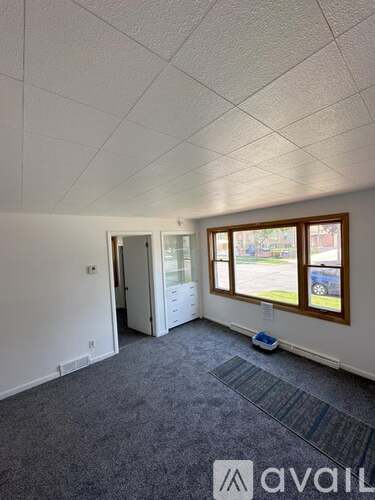 A room with a carpeted floor and a window showing a parking lot outside.