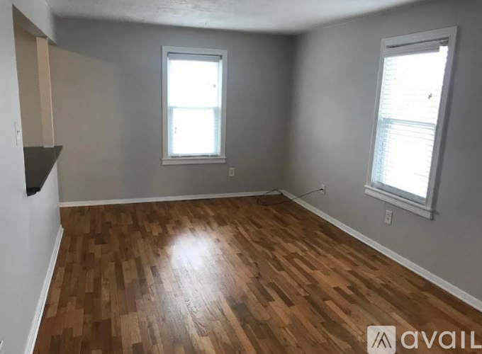 A room with wooden flooring and two windows.