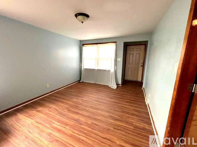 A room with wooden flooring and a window with white curtains.
