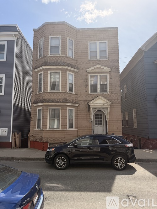 A black car is parked in front of a three-story building.