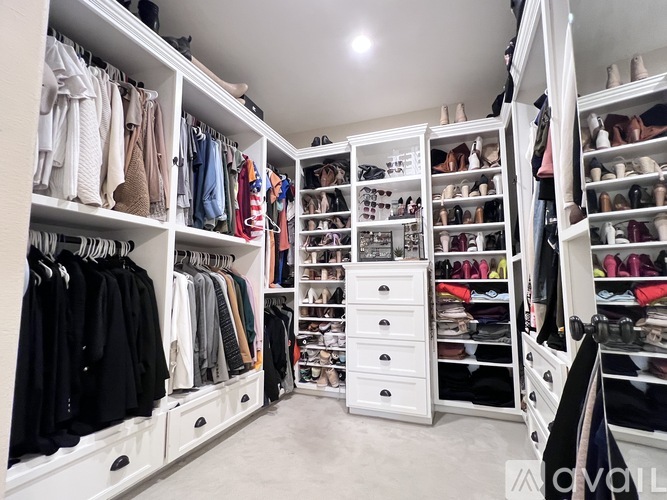 A spacious walk-in closet with white shelving and drawers, organized with clothes and shoes.