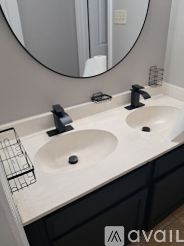 A bathroom with two sinks and a round mirror.