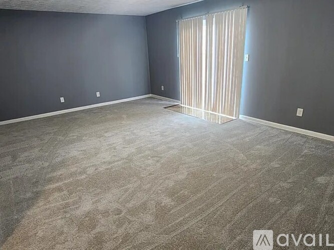 A room with a carpeted floor and a window with blinds.