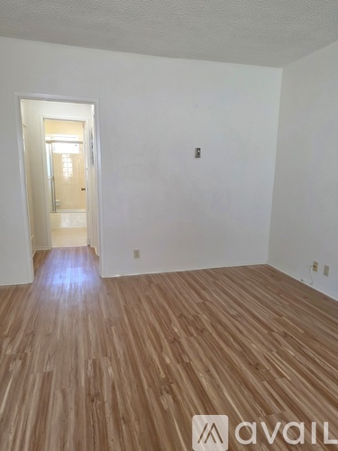 A room with wooden flooring and a doorway leading to another room.