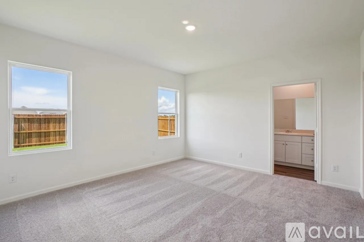 A spacious room with a carpeted floor and two windows overlooking a wooden fence.