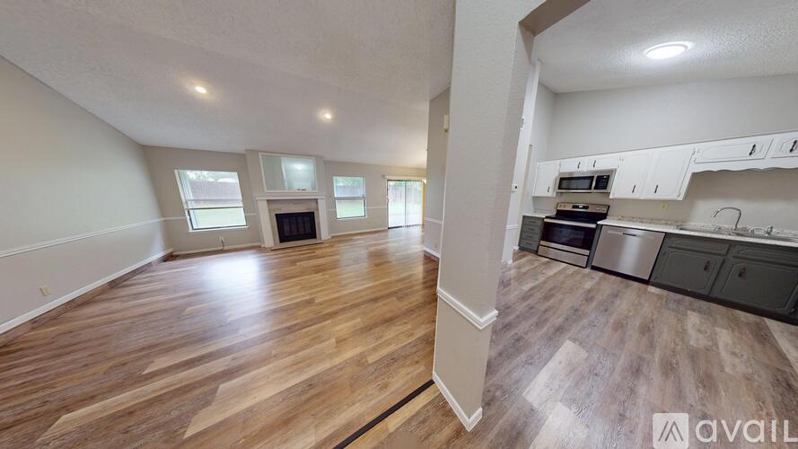 A spacious room with wooden flooring and a kitchen area with stainless steel appliances.