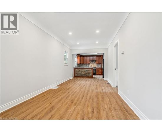 A long hallway with wood floors and a kitchen area in the distance.