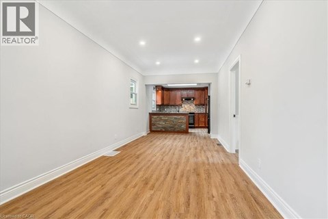 A long hallway with wood floors and a kitchen area in the distance.