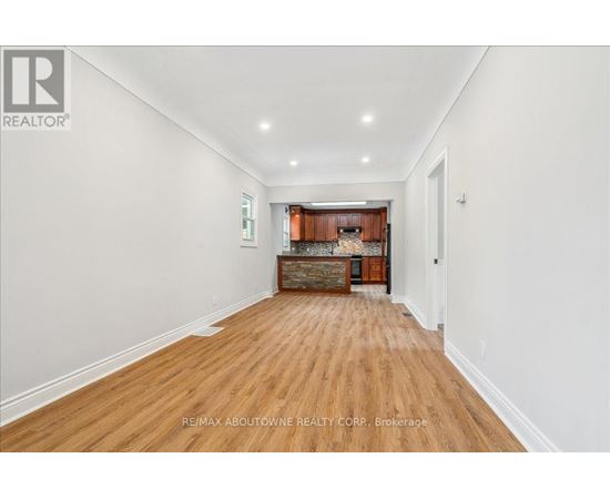 A spacious room with wooden flooring and a kitchen area in the background.